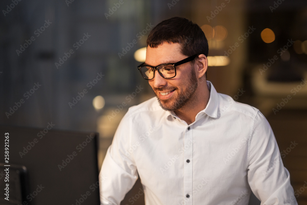 business, overwork, deadline and people concept - happy businessman in glasses with computer working at night office business, overwork, deadline and people concept - happy businessman in glasses with computer working at night office