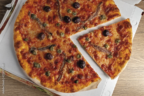 pizza pomodoro acciughe capperi olive nere tagliata dall'alto nella scatola