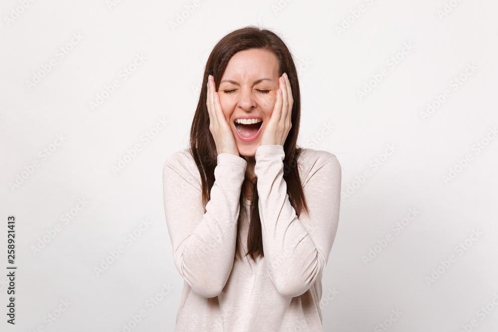 Portrait of cheerful young woman in light clothes keeping eyes closed, putting hands on cheeks isolated on white background in studio. People sincere emotions, lifestyle concept. Mock up copy space. Portrait of cheerful young woman in light clothes keeping eyes closed, putting hands on cheeks isolated on white background in studio. People sincere emotions, lifestyle concept. Mock up copy space.