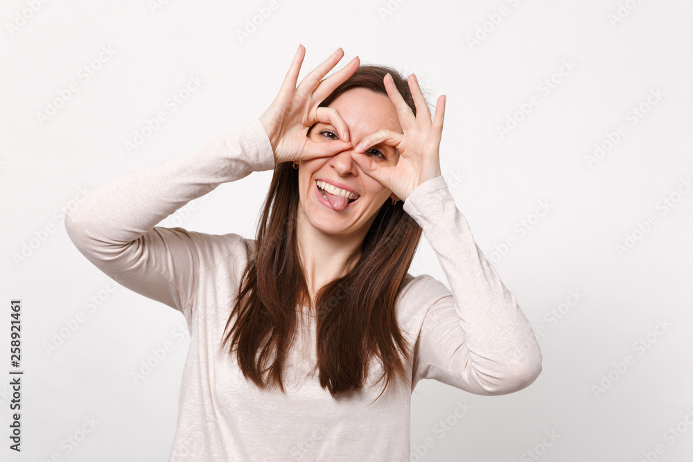 Funny young woman in light clothes holding hands near eyes, imitating glasses or binoculars showing tongue isolated on white background. People sincere emotions, lifestyle concept. Mock up copy space. Funny young woman in light clothes holding hands near eyes, imitating glasses or binoculars showing tongue isolated on white background. People sincere emotions, lifestyle concept. Mock up copy space.