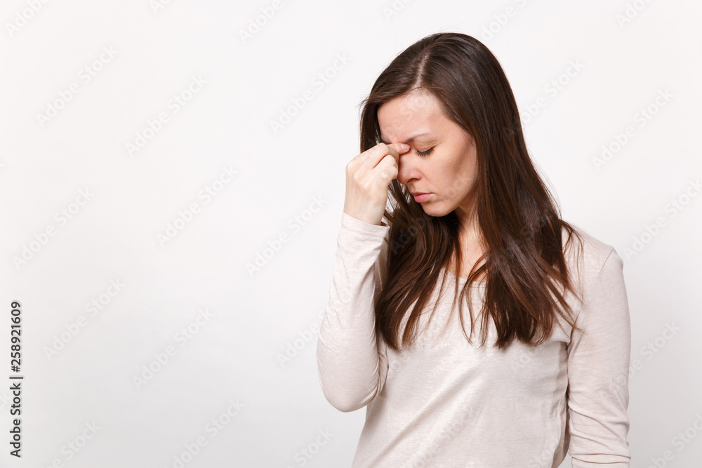 Portrait of tired young woman in light clothes keeping eyes closed, putting hand on nose isolated on white wall background in studio. People sincere emotions lifestyle concept. Mock up copy space. Portrait of tired young woman in light clothes keeping eyes closed, putting hand on nose isolated on white wall background in studio. People sincere emotions lifestyle concept. Mock up copy space.
