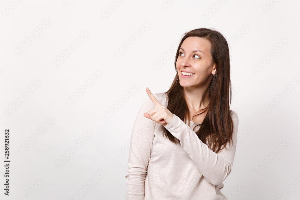 Portrait of smiling young woman in light clothes looking, pointing index finger aside up isolated on white wall background in studio. People sincere emotions, lifestyle concept. Mock up copy space. Portrait of smiling young woman in light clothes looking, pointing index finger aside up isolated on white wall background in studio. People sincere emotions, lifestyle concept. Mock up copy space.