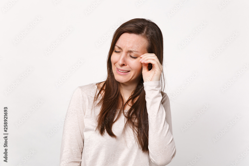 Portrait of displeased upset crying young woman in light clothes wiping tears with hand isolated on white wall background in studio. People sincere emotions lifestyle concept. Mock up copy space.