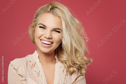 Nice woman with blonde curly bob hairstyle and pretty smile having fun and laughing against colorful pink wall background
