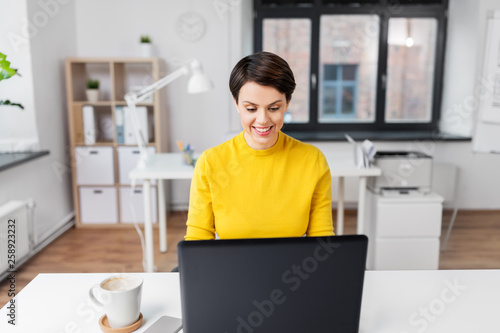 business, technology and people concept - smiling businesswoman with laptop computer working at office