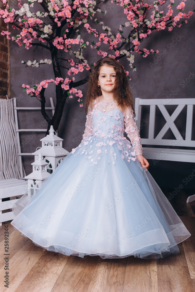 Cute adorable baby girl in elegant blue wedding dress indoors posing and looking at camera. Childhood, fashion kids concept