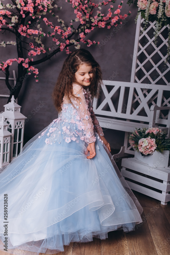 Fototapeta premium Cute adorable baby girl in elegant blue wedding dress indoors posing and looking at camera. Childhood, fashion kids concept