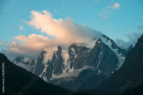 Low cloud above huge glacier. Giant snowy mountains under blue sky. Thick mist in mountains at early morning. Impenetrable fog. Cold rocks. Beautiful calm atmospheric landscape. Tranquil atmosphere.