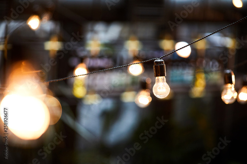 Close-up of bright illuminated bulbs hanging on twisted cables in darkness, design concept