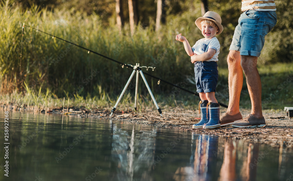 A father with a small toddler son outdoors fishing by a lake. A father with a small toddler son outdoors fishing by a lake.
