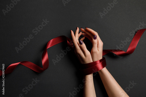 Fotografie cropped view of woman tied with silk red ribbon on black background