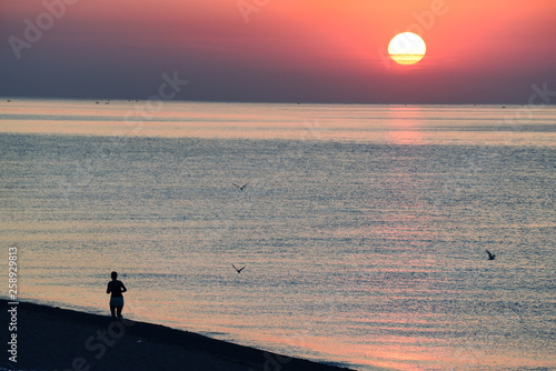 a woman doing a run through the sea ebregu at dawn. The sun rises above the surface of the sea 
