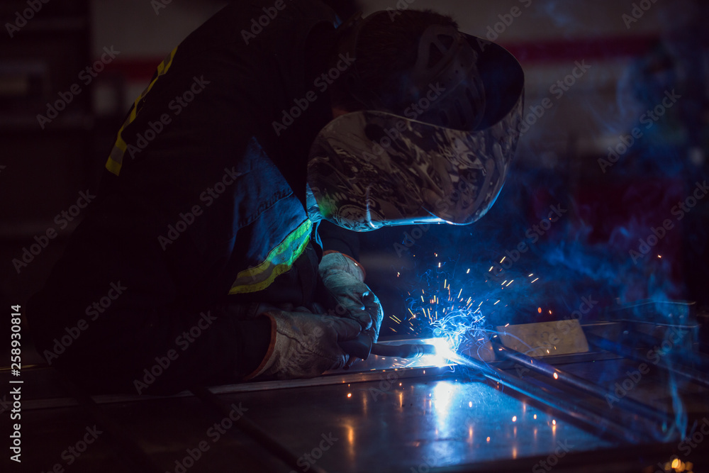 Worker grinding on a metal gate, at his workshop, wearing safety helmet Worker grinding on a metal gate, at his workshop, wearing safety helmet