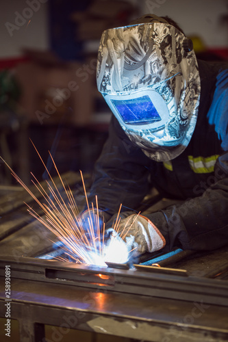 Worker grinding on a metal gate, at his workshop, wearing safety helmet