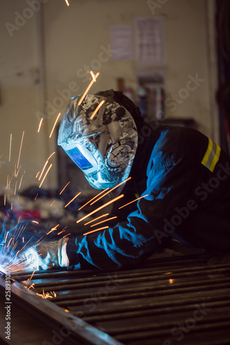 Worker grinding on a metal gate, at his workshop, wearing safety helmet