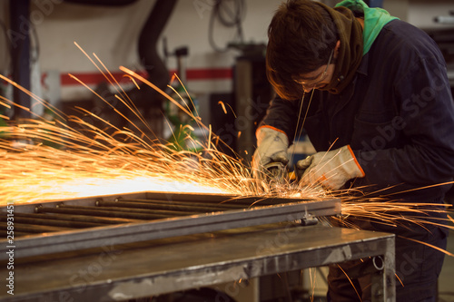 Worker grinding on a metal gate, at his workshop, wearing safety glasses