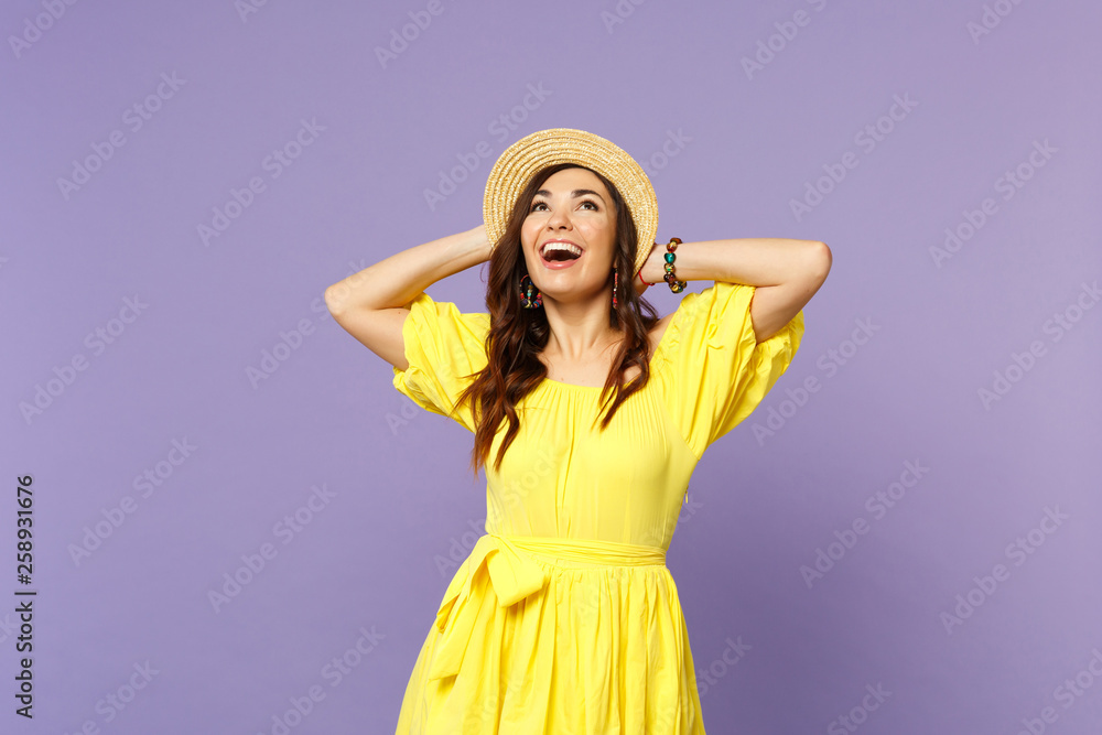 Cheerful young woman in yellow dress, hat looking up, keeping mouth open, putting hands behind head isolated on pastel violet background. People sincere emotions lifestyle concept. Mock up copy space. Cheerful young woman in yellow dress, hat looking up, keeping mouth open, putting hands behind head isolated on pastel violet background. People sincere emotions lifestyle concept. Mock up copy space.