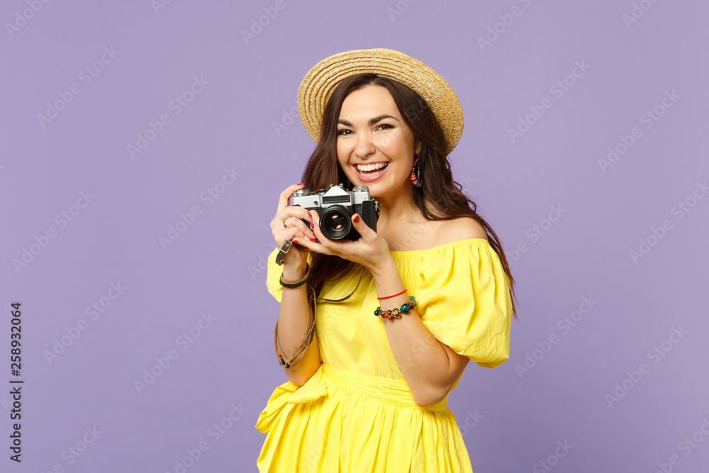 Cheerful young woman in yellow dress, summer hat taking pictures on retro vintage photo camera isolated on pastel violet wall background. People sincere emotions lifestyle concept. Mock up copy space.