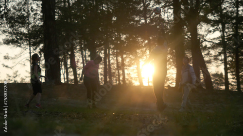 Friends play volleyball in forest during sunset