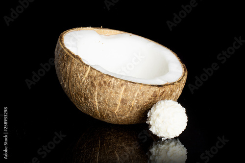 One half of fresh bio coconut with a small cocoa ball isolated on black glass