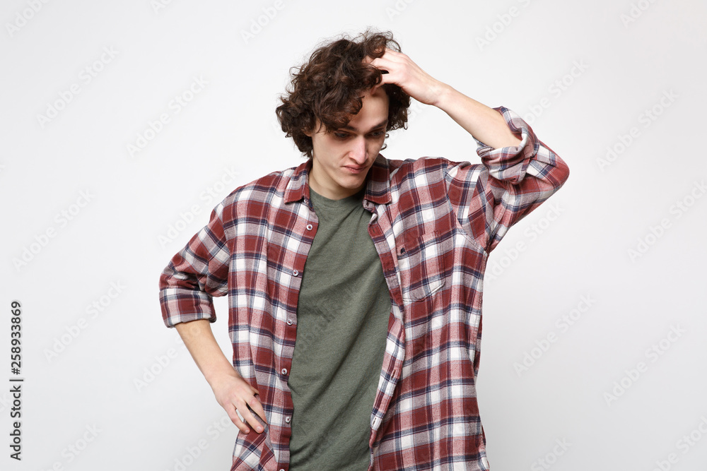 Portrait of preoccupied upset young man in casual clothes looking down putting hand on head isolated on white wall background in studio. People sincere emotions, lifestyle concept. Mock up copy space. Portrait of preoccupied upset young man in casual clothes looking down putting hand on head isolated on white wall background in studio. People sincere emotions, lifestyle concept. Mock up copy space.