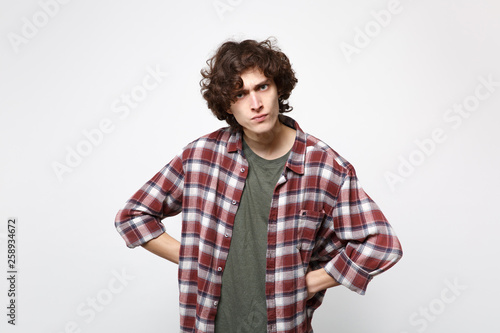 Portrait of angry strict young man in casual clothes standing with arms akimbo on waist isolated on white wall background in studio. People sincere emotions, lifestyle concept. Mock up copy space.