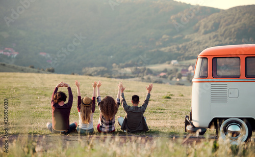 A rear view of group of young friends sitting on grass on a roadtrip through countryside. photo