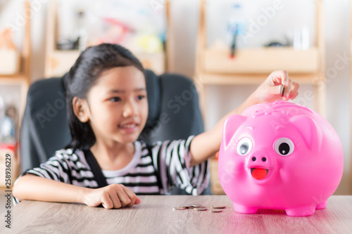 Asian little girl in putting coin in to piggy bank shallow depth of field select focus at the pig