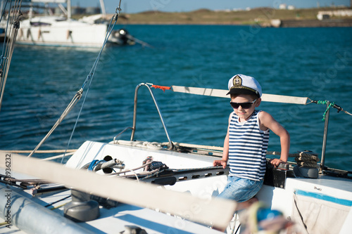 strong little caucasian boy in sunglasses and captain cap on white yacht board during sailing