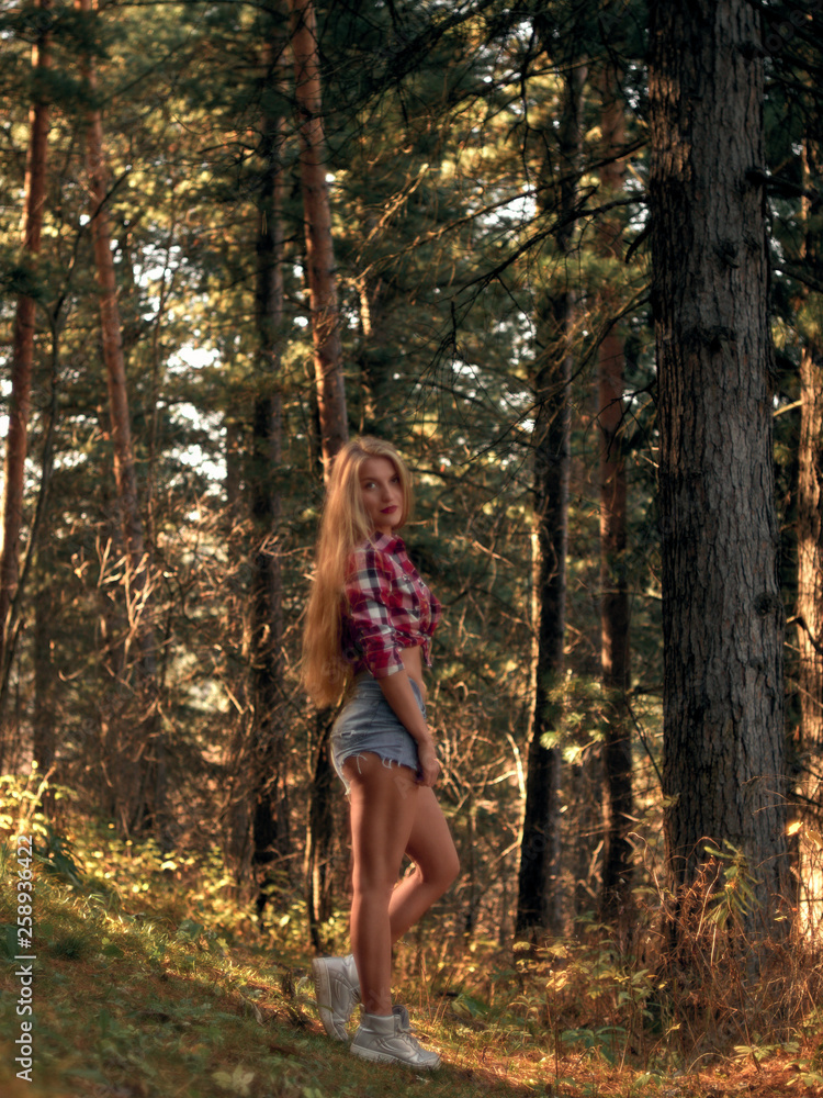 Slim athletic blonde in shorts and a plaid shirt in a pine forest. Slim athletic blonde in shorts and a plaid shirt in a pine forest.