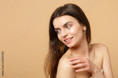 Close up half naked woman 20s with perfect skin, nude make up patches under eyes isolated on beige pastel wall background, studio portrait. Health care cosmetic procedures concept. Mock up copy space.