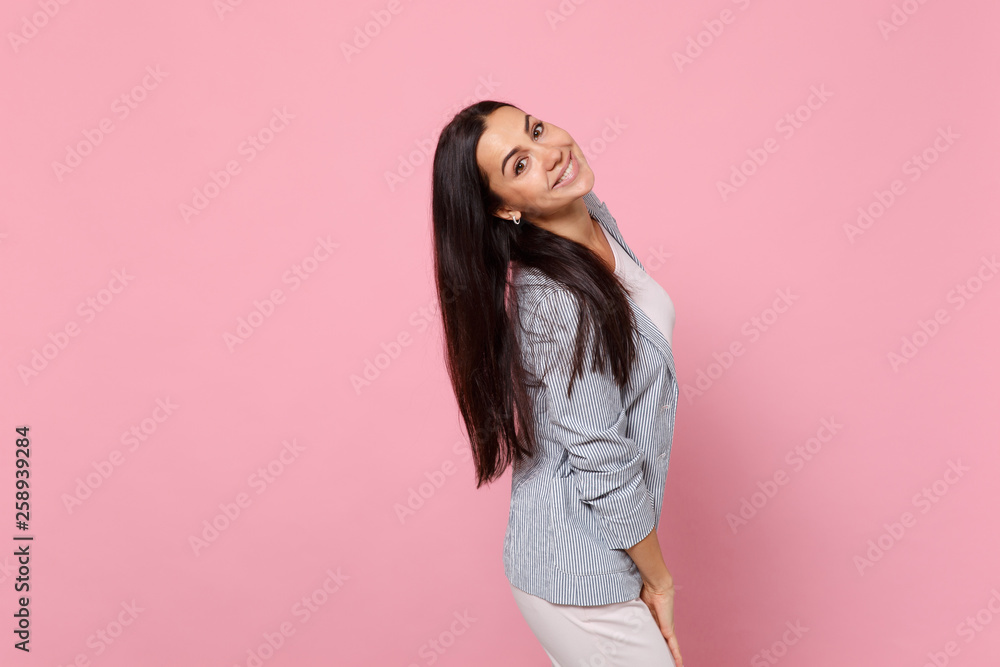 Side view of smiling cheerful young woman in striped jacket standing, looking camera isolated on pink pastel wall background in studio. People sincere emotions lifestyle concept. Mock up copy space. Side view of smiling cheerful young woman in striped jacket standing, looking camera isolated on pink pastel wall background in studio. People sincere emotions lifestyle concept. Mock up copy space.