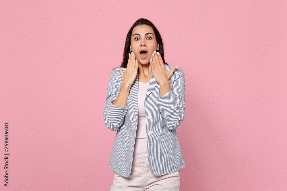 Shocked young woman in striped jacket keeping mouth wide open keeping hands nead mouth isolated on pink pastel wall background in studio. People sincere emotions lifestyle concept. Mock up copy space. Shocked young woman in striped jacket keeping mouth wide open keeping hands nead mouth isolated on pink pastel wall background in studio. People sincere emotions lifestyle concept. Mock up copy space.