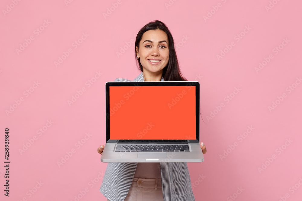 Portrait of smiling young woman in striped jacket holding laptop pc computer with blank empty screen isolated on pink pastel background. People sincere emotions, lifestyle concept. Mock up copy space. - obrazy, fototapety, plakaty 