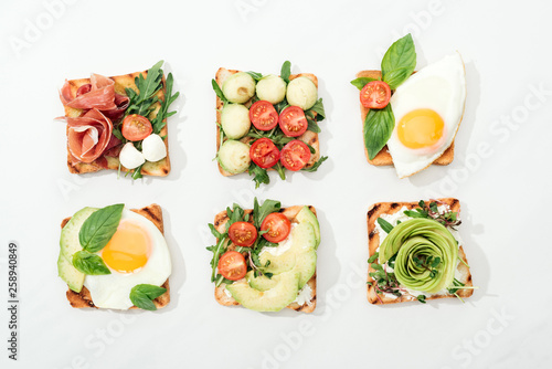 Fototapeta Naklejka Na Ścianę i Meble -  Top view of toasts with cut vegetables and prosciutto on white surface
