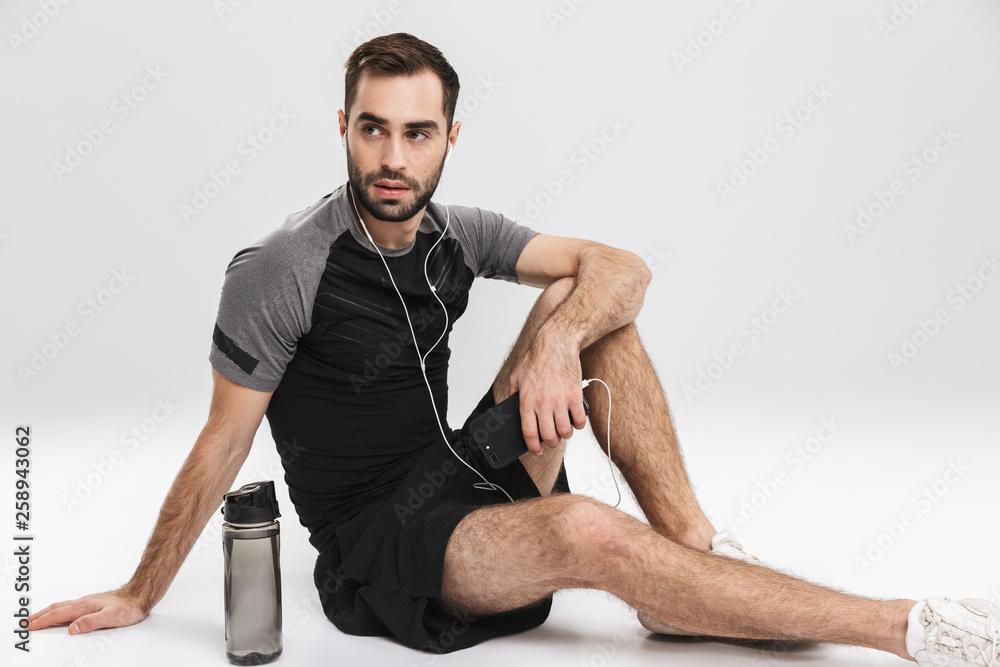 Handsome young sports fitness man posing isolate over white wall background listening music with earphones. Handsome young sports fitness man posing isolate over white wall background listening music with earphones.