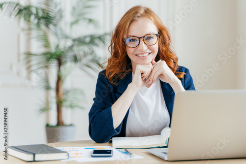 Photos Pleased cheerful red haird female economist develops financial startup project,
