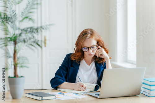 Obraz na plátne Serious confident female entrepreneur in formal clothes writes down information
