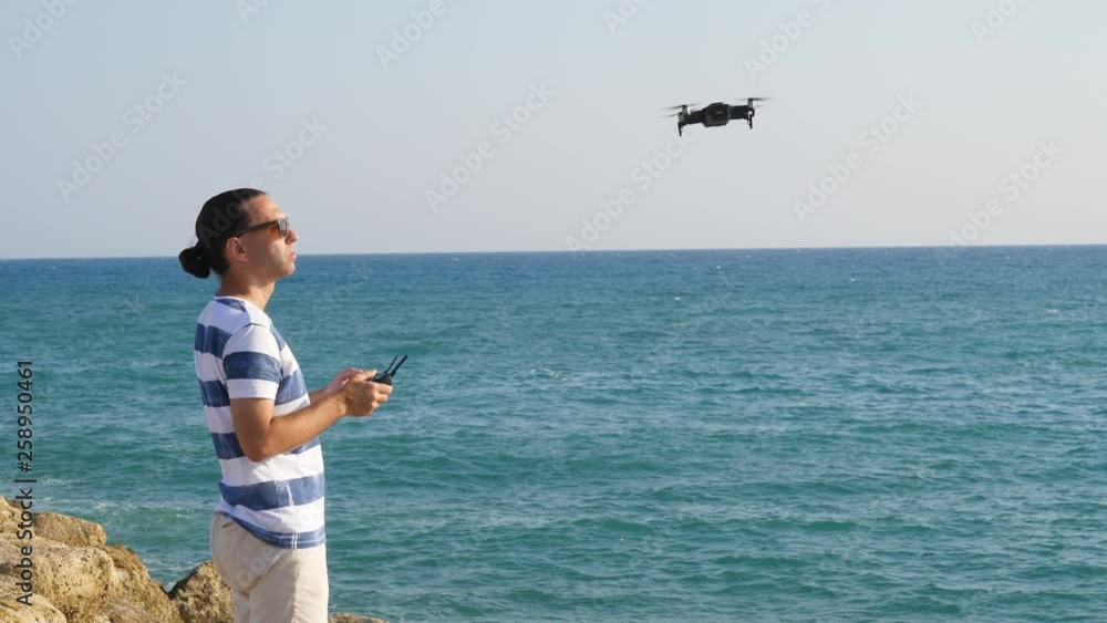 Man operate small flying quadcopter at sea shore, windy weather Man operate small flying quadcopter at sea shore, windy weather