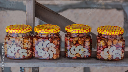 On a wooden shelf there are banks with multi-colored syrups from various nuts collected in the mountain forest of the Caucasus. Natural product. Delicacy with original taste. Food photography. © mangz