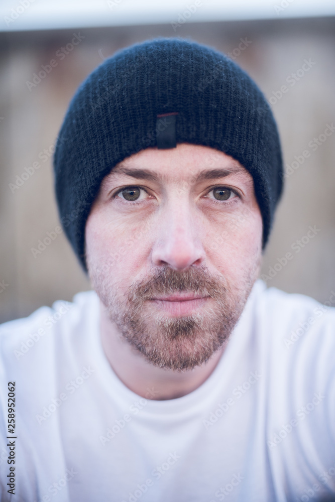 A portrait of young handsome man with stubble and a beanie hat standing alone and contemplating life by the quiet sea, surrounded by raw concrete sea defence wall. A portrait of young handsome man with stubble and a beanie hat standing alone and contemplating life by the quiet sea, surrounded by raw concrete sea defence wall.