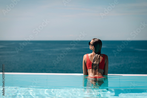 Young woman relaxaing in the swimming pool looking at the ocean view in background l. Beautiful seascape. Trip to warm destination. Phuket. Thailand.