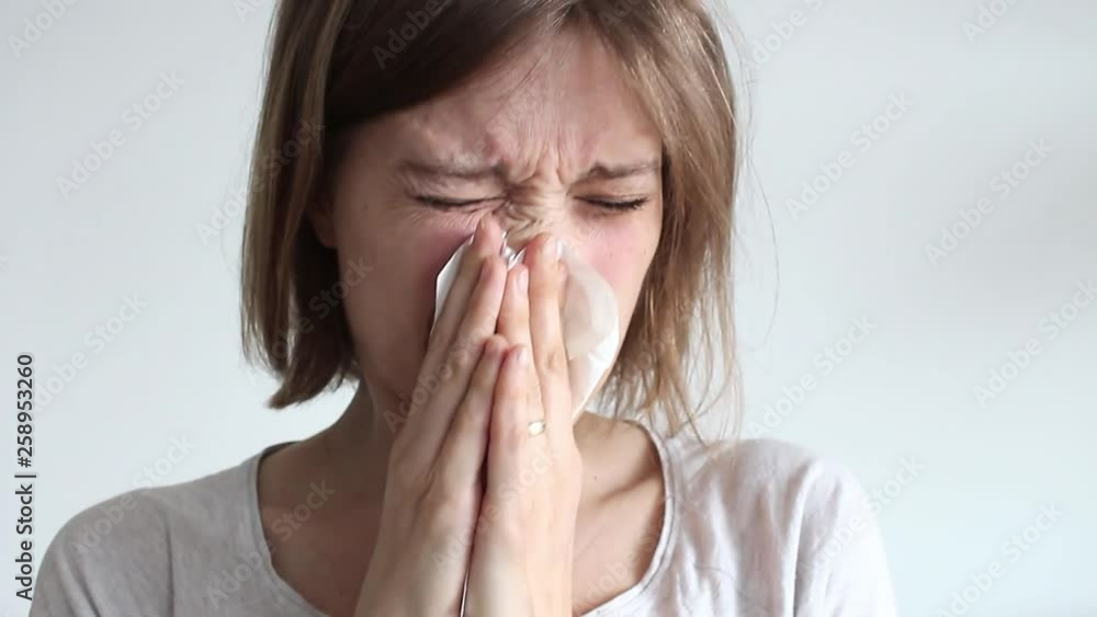 sick young millenial woman blowing nose into white tissue on white background. Young Female having cold or flu symptoms sick young millenial woman blowing nose into white tissue on white background. Young Female having cold or flu symptoms