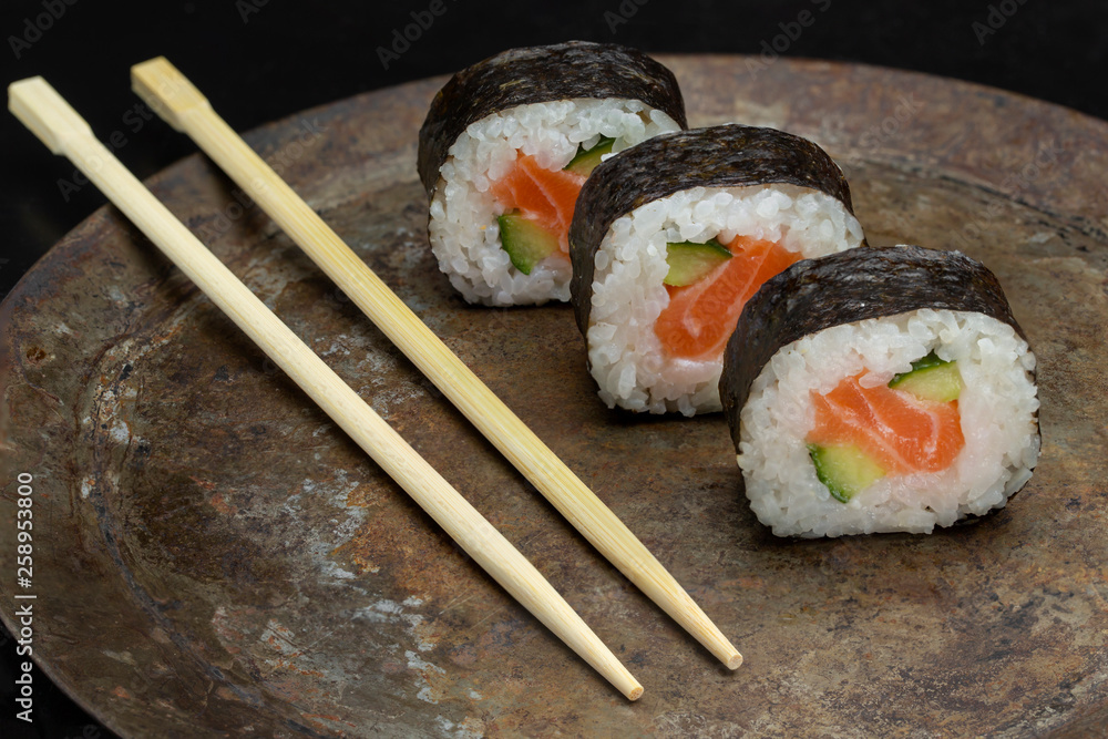 Sushi rolls on a dark metal plate, with chopsticks Sushi rolls on a dark metal plate, with chopsticks