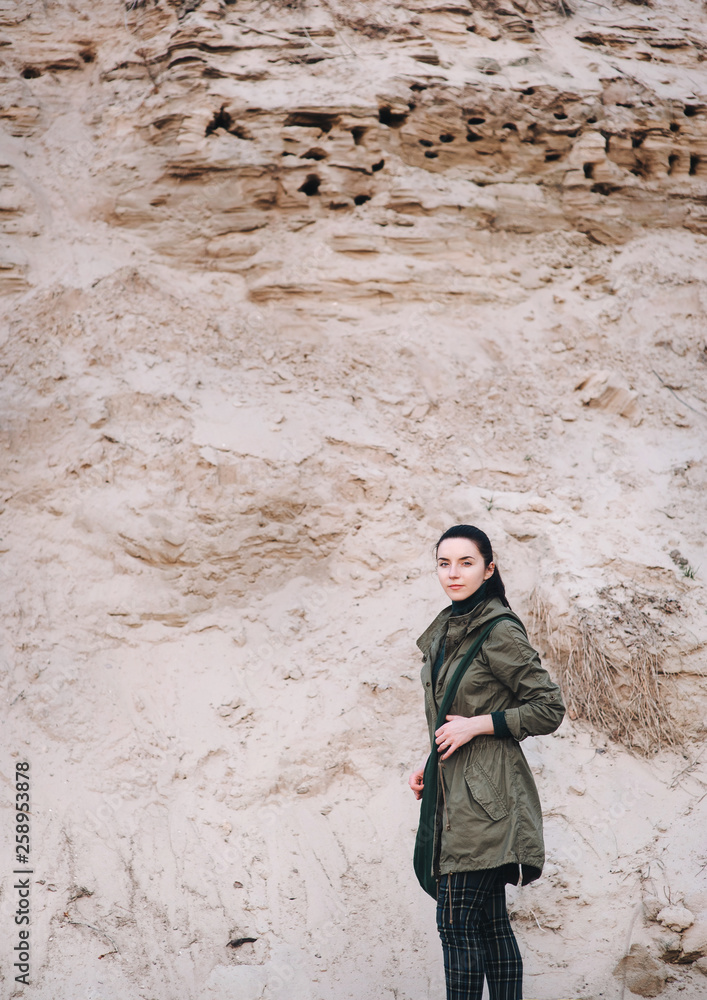 An archaeologist girl in olive-colored clothes stands against a background of sand. Copy space. An archaeologist girl in olive-colored clothes stands against a background of sand. Copy space.