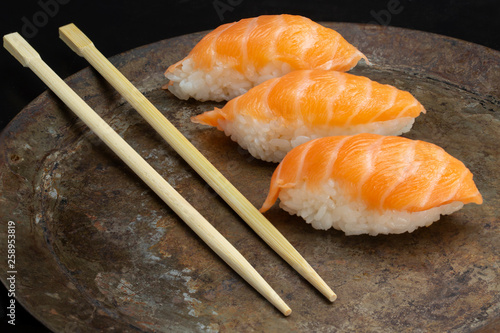Sushi rolls on a dark metal plate, with chopsticks