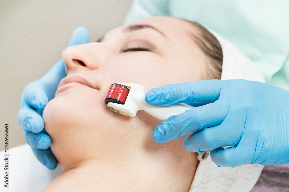 The woman undergoes the procedure of medical micro needle therapy with a modern medical instrument derma roller. The woman undergoes the procedure of medical micro needle therapy with a modern medical instrument derma roller.