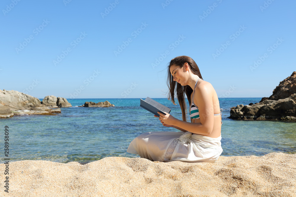 Tourist on the beach reading a paper book in summer