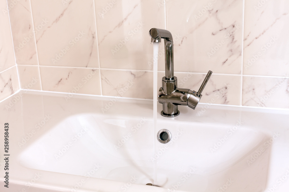 Fototapeta premium Faucet pouring water into white sink