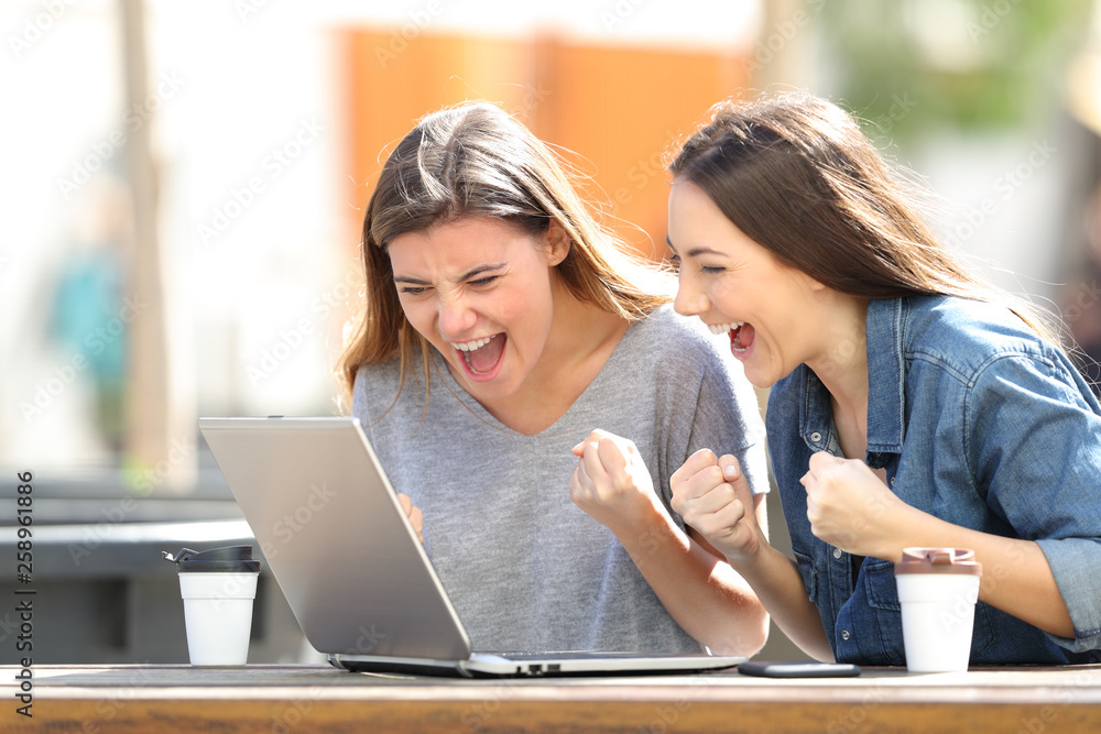 © Antonioguillem - Excited women checking laptop content in a park